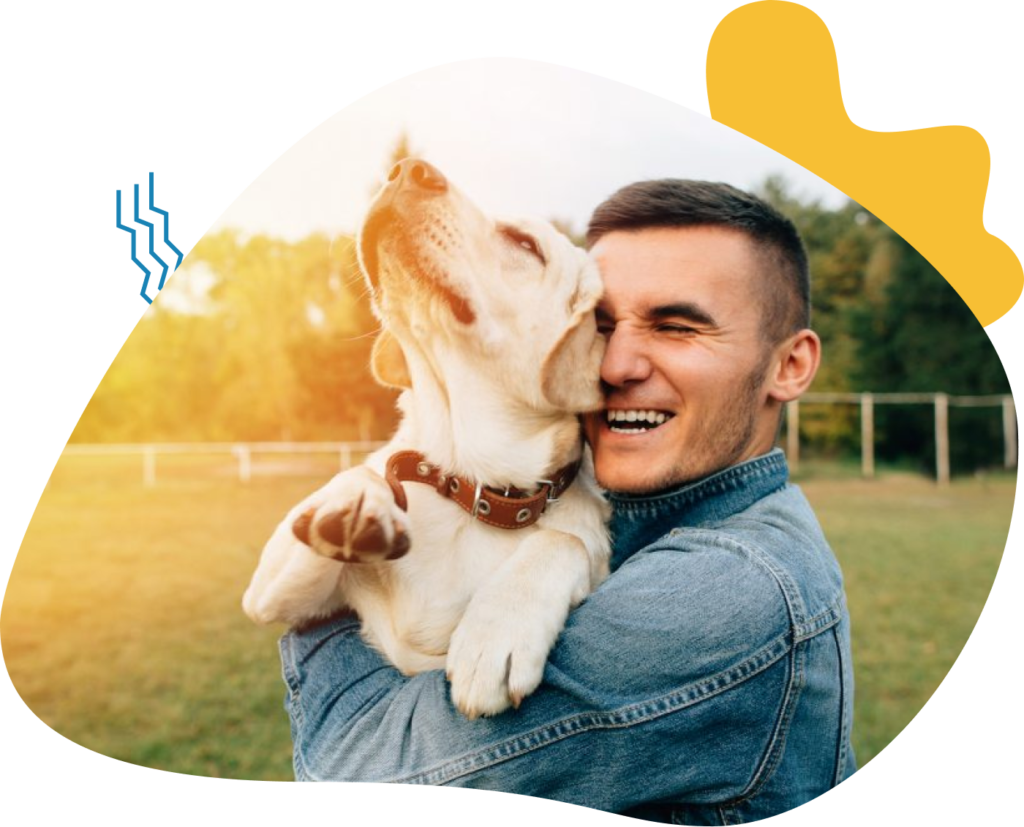 A man joyfully embraces a playful dog outdoors at sunset.