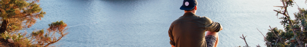Person standing by calm water wearing a brown jacket.